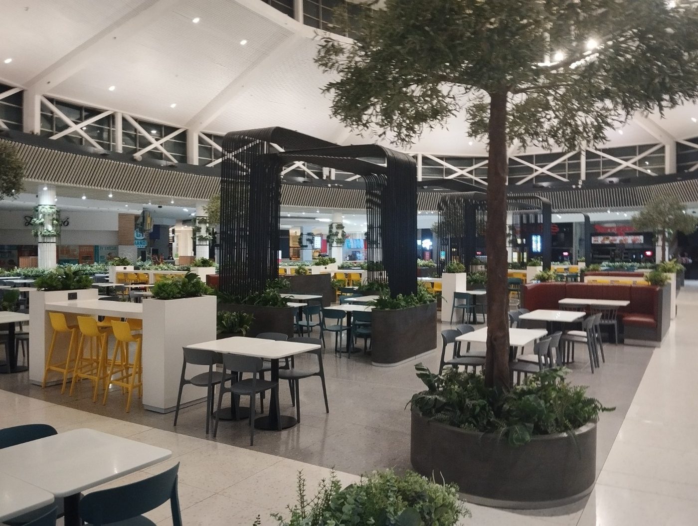 Área de mesas y jardineras en el patio de comidas